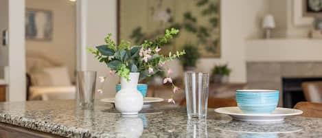 A kitchen counter with a white vase, a clear glass, and a blue bowl on a granite countertop.