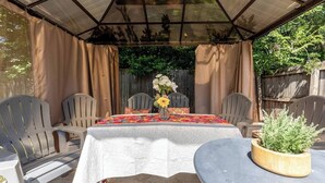 Ein überdachter Patio-Bereich mit einem für zwei Personen gedecktem Tisch, umgeben von Stühlen und einem Blumentopf auf dem Tisch.