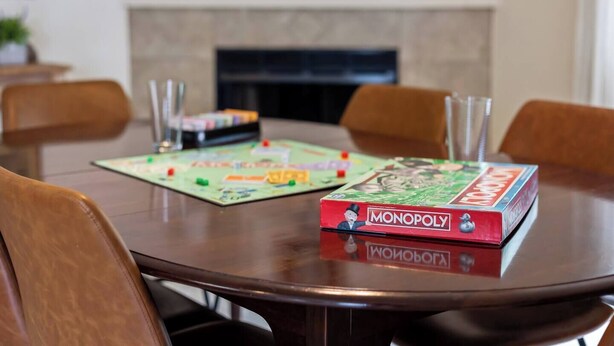Ein Esstisch mit zwei Monopoly-Spielen, Stühlen darum herum und einem Kamin im Hintergrund.