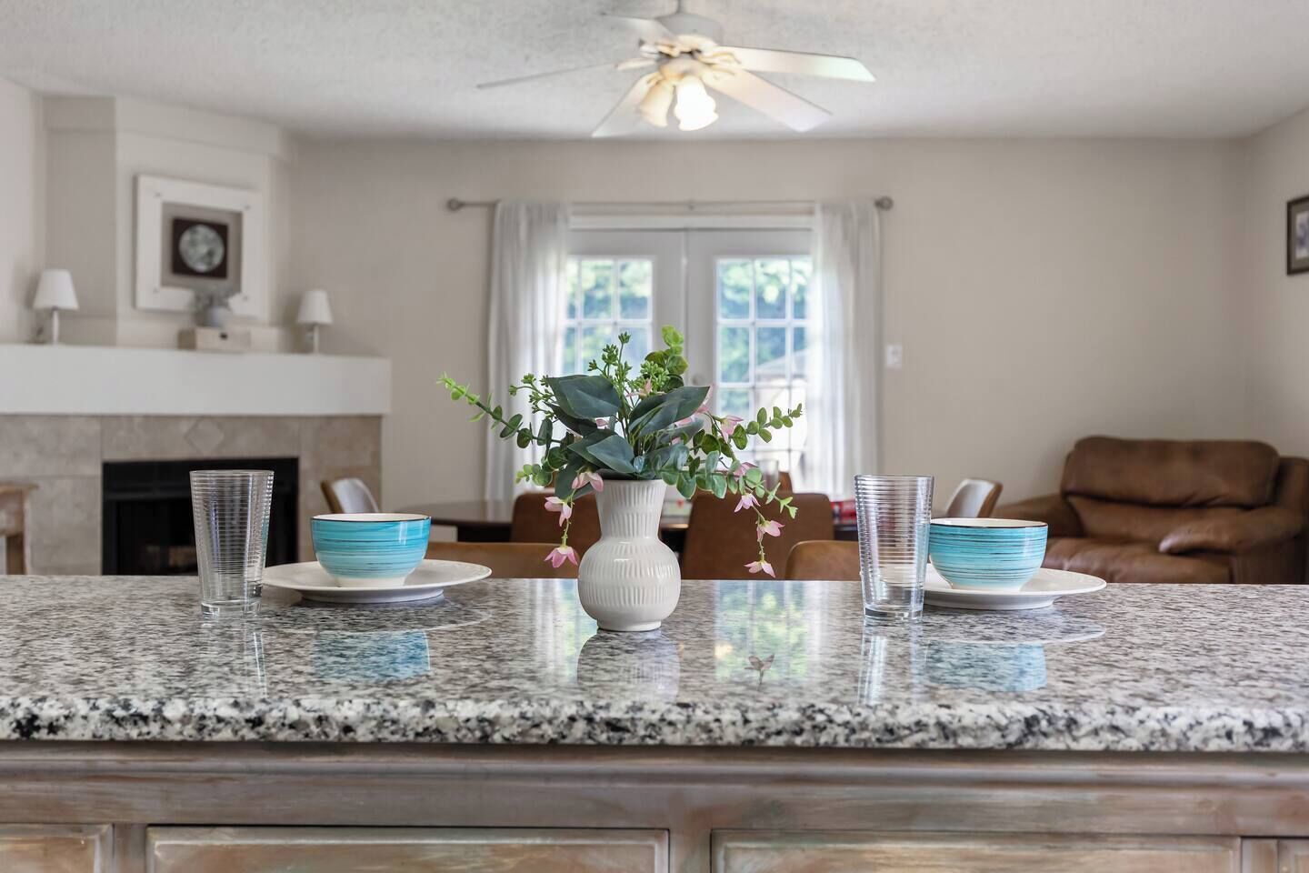 A kitchen with granite countertops, a white vase with flowers, and a dining area with a brown leather chair.