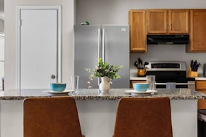 Eine Küche mit Granit-Arbeitsplatten, Holzschränken, einem Edelstahlkühlschrank und einer Vase mit Blumen auf der Kücheninsel.