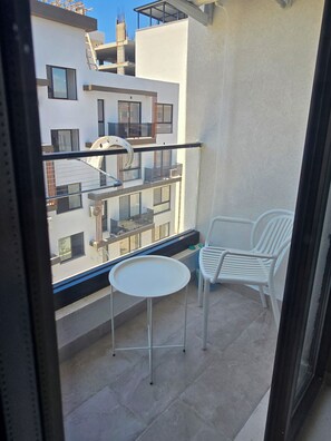 A balcony with a table and two chairs, overlooking a modern building with multiple floors and balconies. - Sea & Sun Studio! A warm place for your holidays! 300 m from the Sea. (Golem)