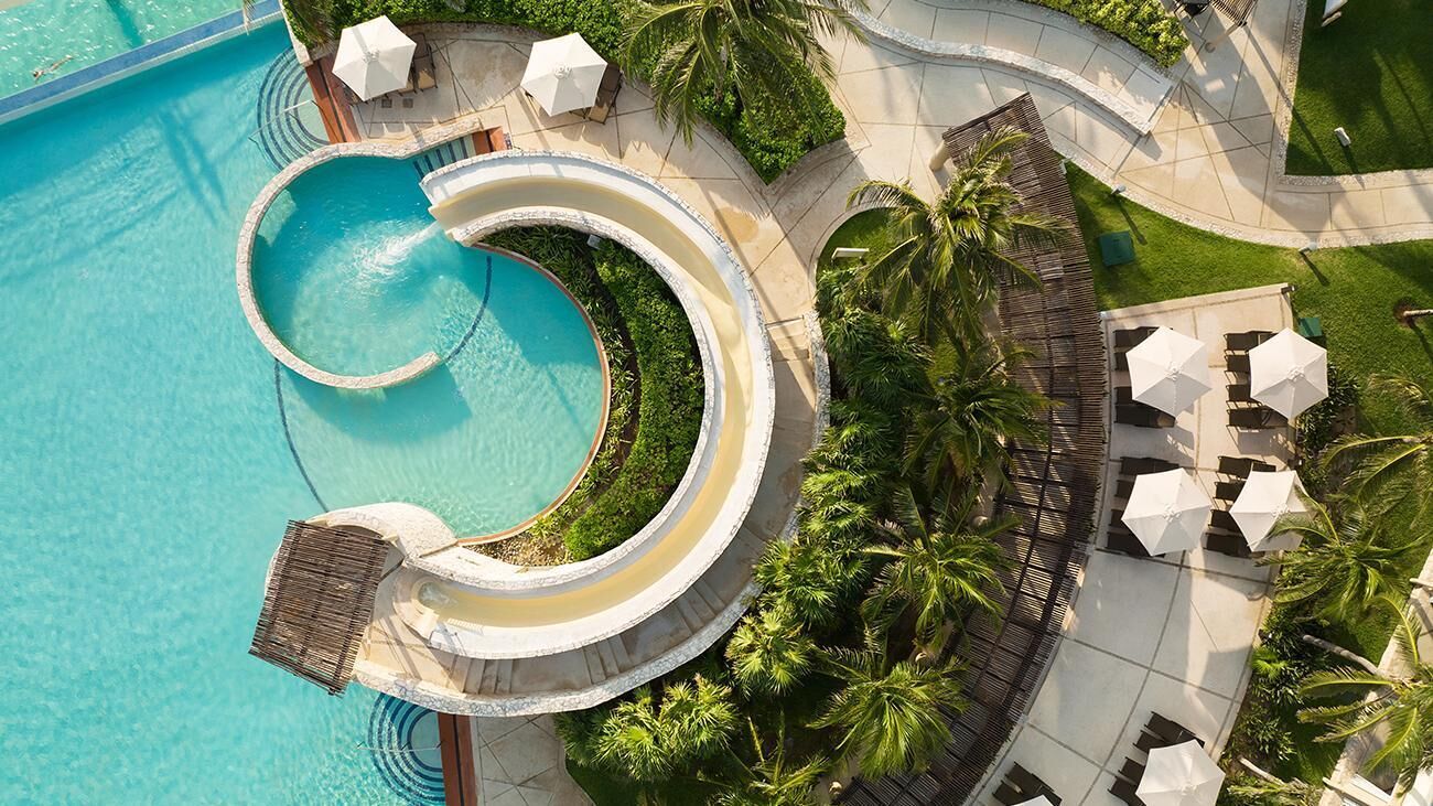 Ein Resort mit großem, kreisförmigen Pool, Palmen und Sitzgelegenheiten im Freien.