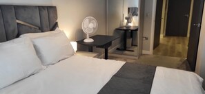 A hotel room with a bed, a bedside table with a lamp, and a standing fan. - Cozy Central London, Zone 1 Apartment, Sleeps 5 (London)
