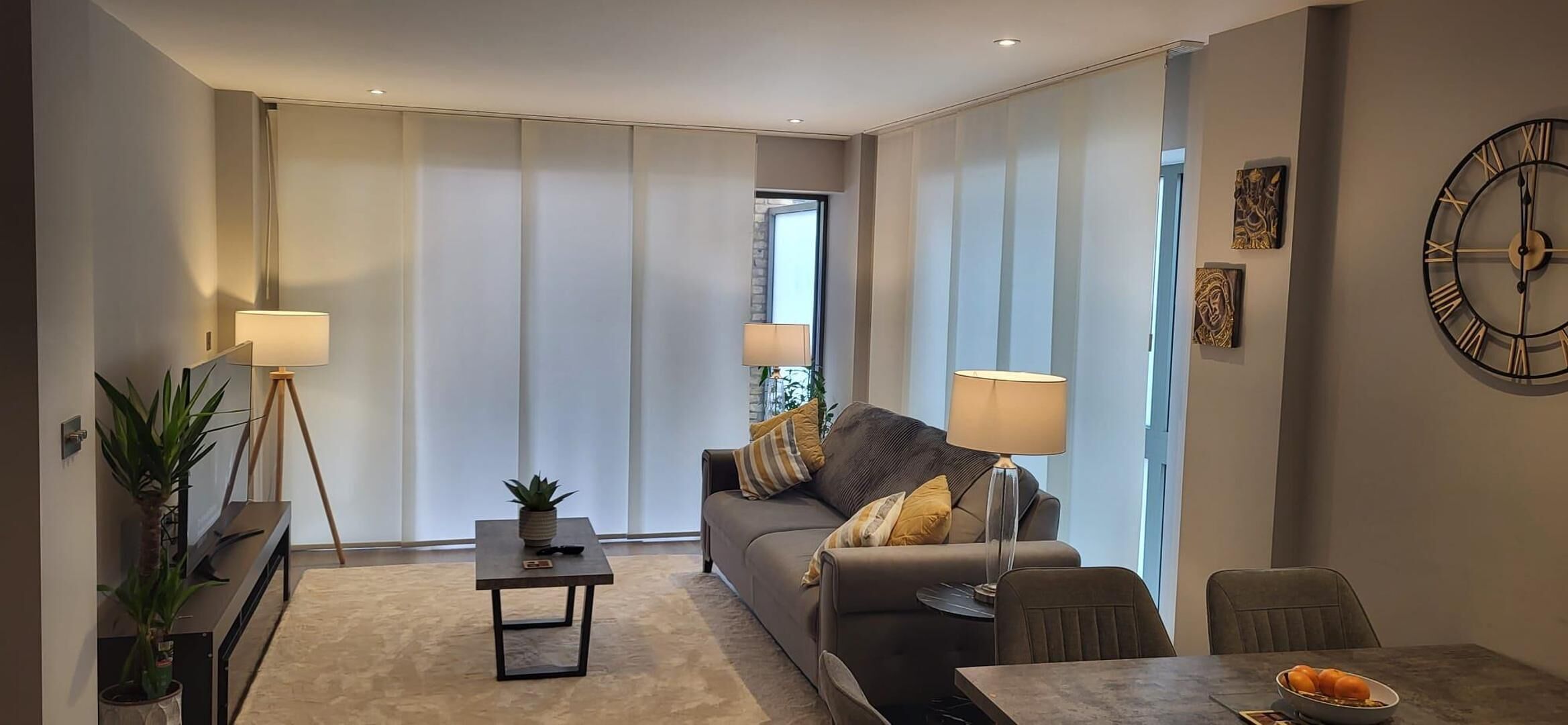 A modern living room with a sofa, a coffee table, a lamp, and a dining area with a table and chairs.