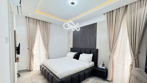 Une chambre moderne avec un grand lit, une table de chevet, un téléviseur fixé au mur et un luminaire au plafond.