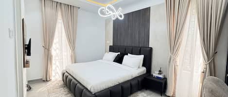 Un dormitorio moderno con una cama grande, una mesita de noche, un televisor montado en la pared y una lámpara del techo.