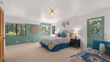 A bedroom with a large bed, a smaller bed, a nightstand, a lamp, a wall hanging, and a door.