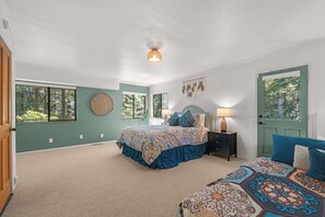 Ein Schlafzimmer mit einem großen Bett, einem kleineren Bett, einem Nachttisch, einer Lampe, einer Wanddekoration und einer Tür.