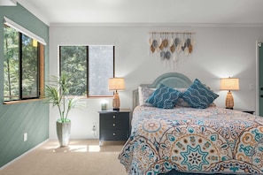 A bedroom with a bed, two bedside lamps, a nightstand, a potted plant, and a window with a view of trees. - 3BR Gualala Forest Retreat | Game Room, Soaking Tub & ADU Suite (Mendocino County)