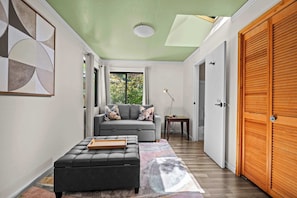 A modern living room with a grey sofa, a black ottoman, and a wooden sideboard. - 3BR Gualala Forest Retreat | Game Room, Soaking Tub & ADU Suite (Mendocino County)