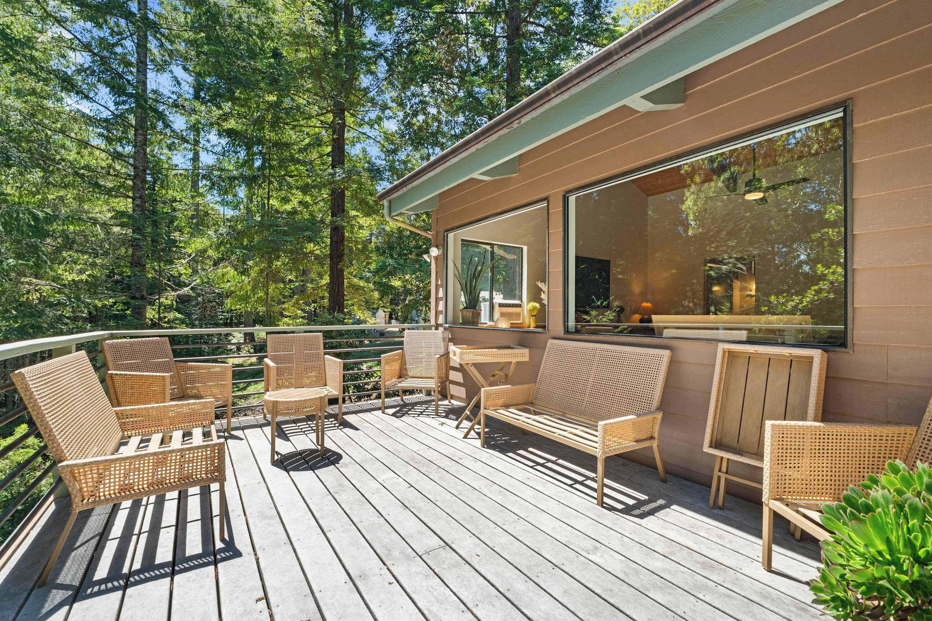 A wooden deck with wicker furniture and large windows overlooking a forest.