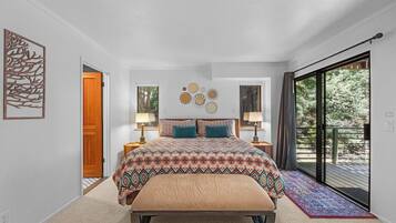 A bedroom with a large bed, a bench, a door, and a view of the outdoors.