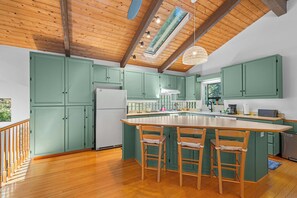 Een keuken met groene kasten, een centraal eiland met barstoelen, houten vloeren en een schuin plafond met dakramen.