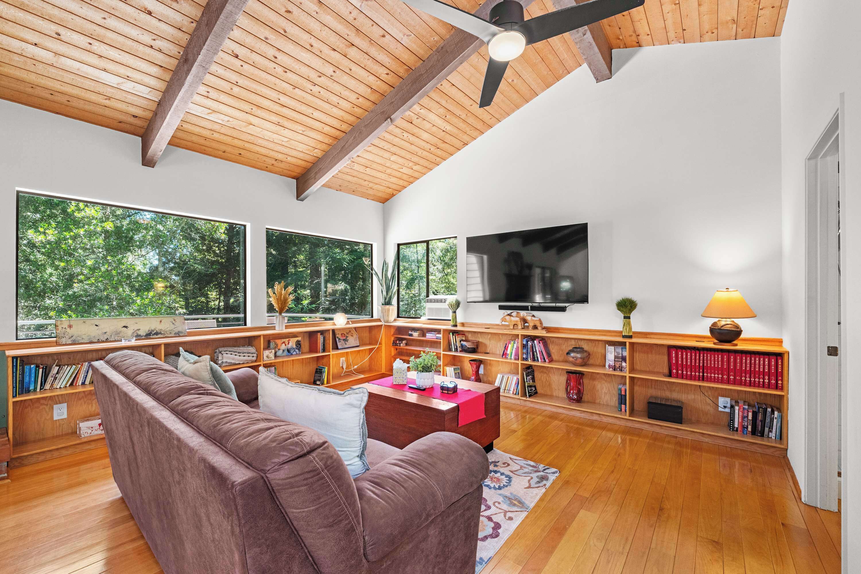 A spacious living room with a high ceiling, wooden beams, a large flat-screen TV, and a cozy seating area with a sofa and bookshelves.