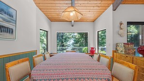 Uma sala de jantar com uma mesa grande, cadeiras e vista para o verde lá fora.