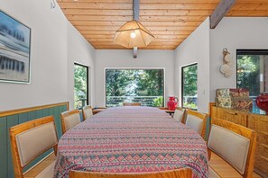 Ein Esszimmer mit großem Tisch, Stühlen und Blick auf Grünfläche.