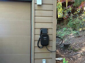 An outdoor electrical outlet mounted on a wooden wall, connected to a black charging cable. - 3BR Gualala Forest Retreat | Game Room, Soaking Tub & ADU Suite (Mendocino County)
