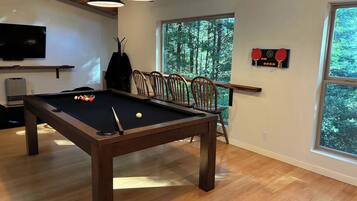 A pool table with balls, a television, and a window with a view of trees.