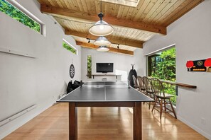 Ein Tischtennis-Tisch in einem Raum mit Holzboden, Deckenbalken und einem an der Wand befestigten Fernseher.
