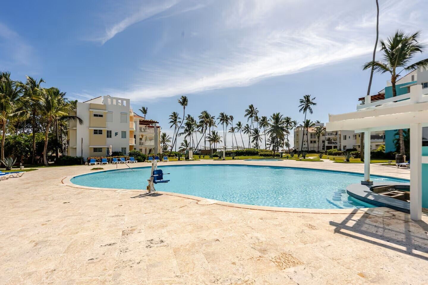 A swimming pool with lounge chairs, palm trees, and hotel buildings in the background.