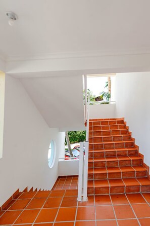 Eine Treppe mit Terrakottafliesen führt zu einer Zwischenebene mit einem weißen Geländer und einem kleinen Fenster.