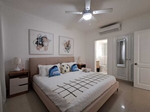 Ein Schlafzimmer mit einem Bett, Nachttischen, einem Deckenventilator und Kunstwerken an der Wand.
