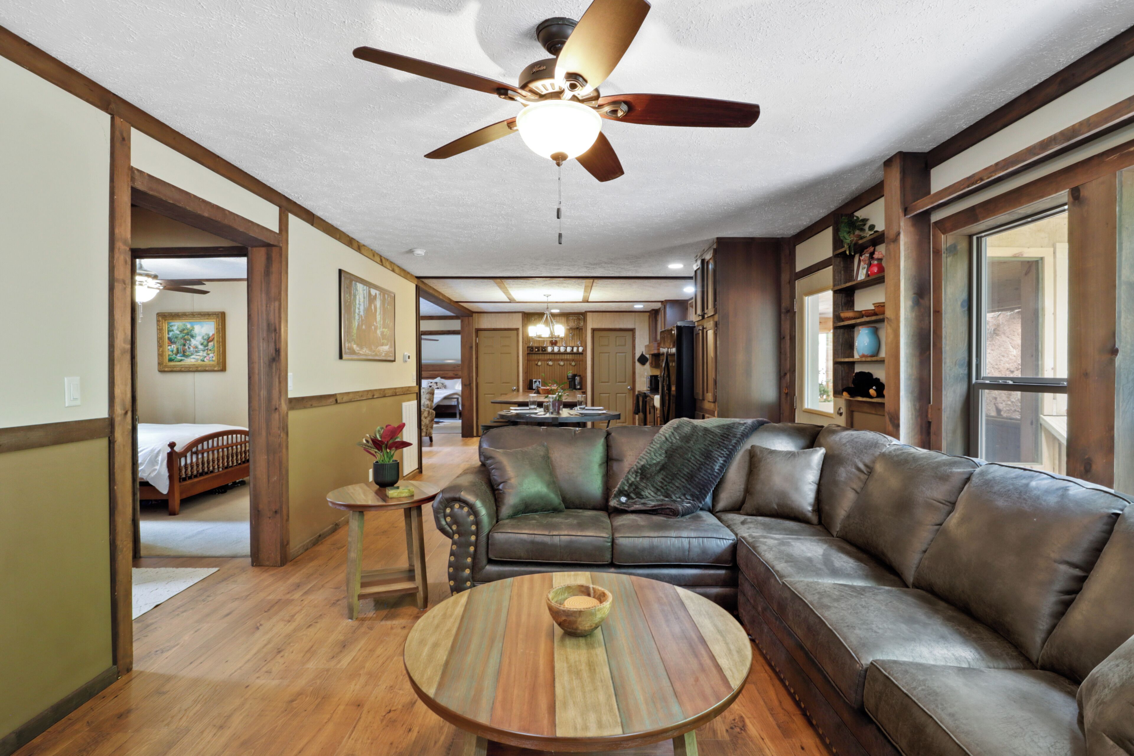 A spacious living room with a large leather sofa, a round wooden coffee table, and a ceiling fan.