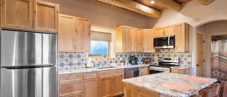 A kitchen with wooden cabinets, stainless steel appliances, a tiled backsplash, and a large island with seating.