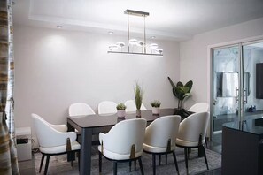 A modern dining area with a rectangular table surrounded by white chairs, a central chandelier, and potted plants. - Charming luxury villa near Disneyland Paris. 6 bedrooms. Air-conditioned. Sleeps 16 (Bussy-Saint-Georges)