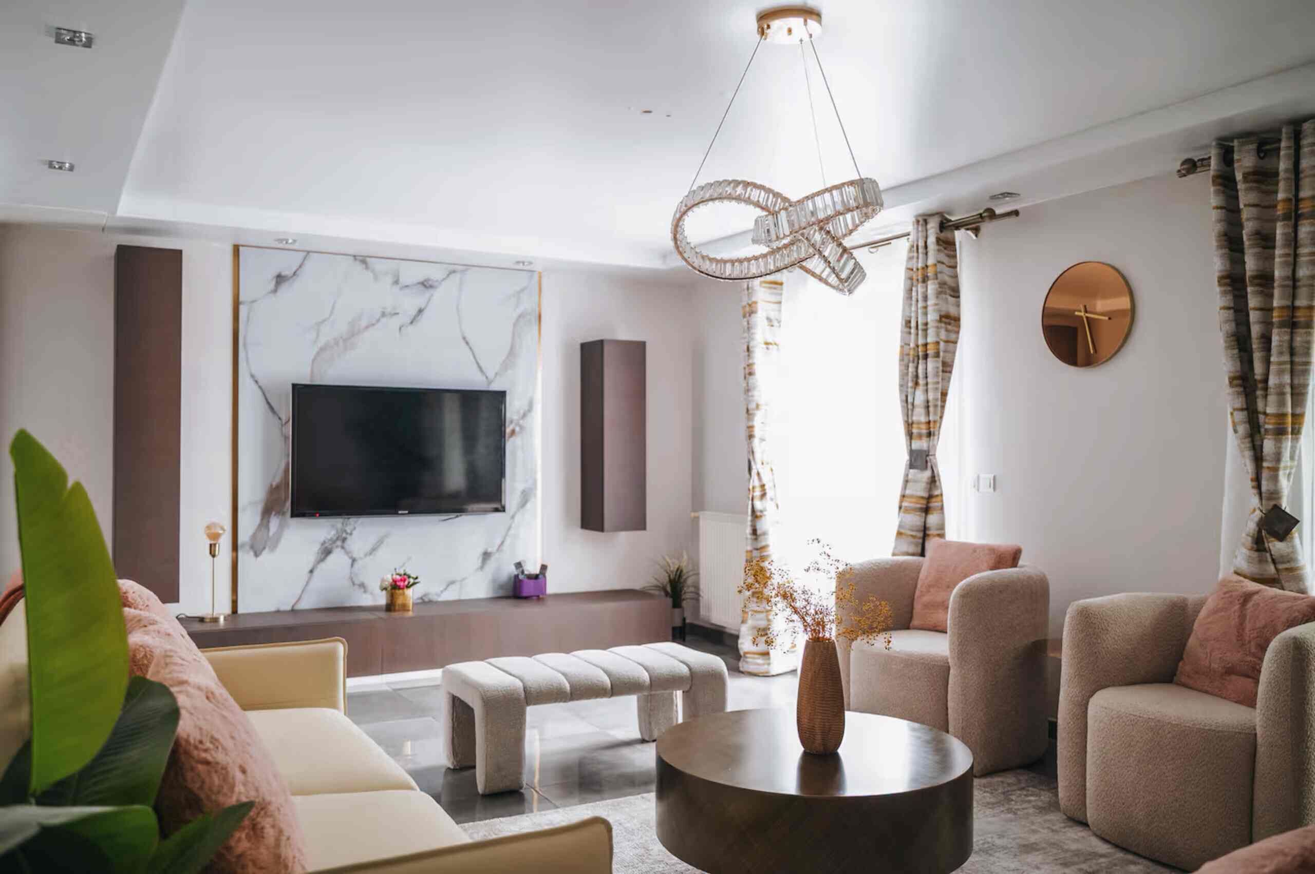 A modern living room with a flat-screen TV, marble wall, and a unique chandelier.