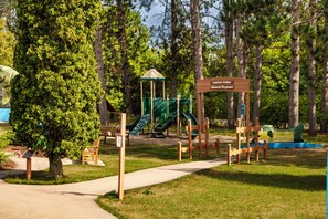 A playground with a slide and climbing structures, surrounded by trees. - Welcome to Lazy Days Lake House. (Hayward)