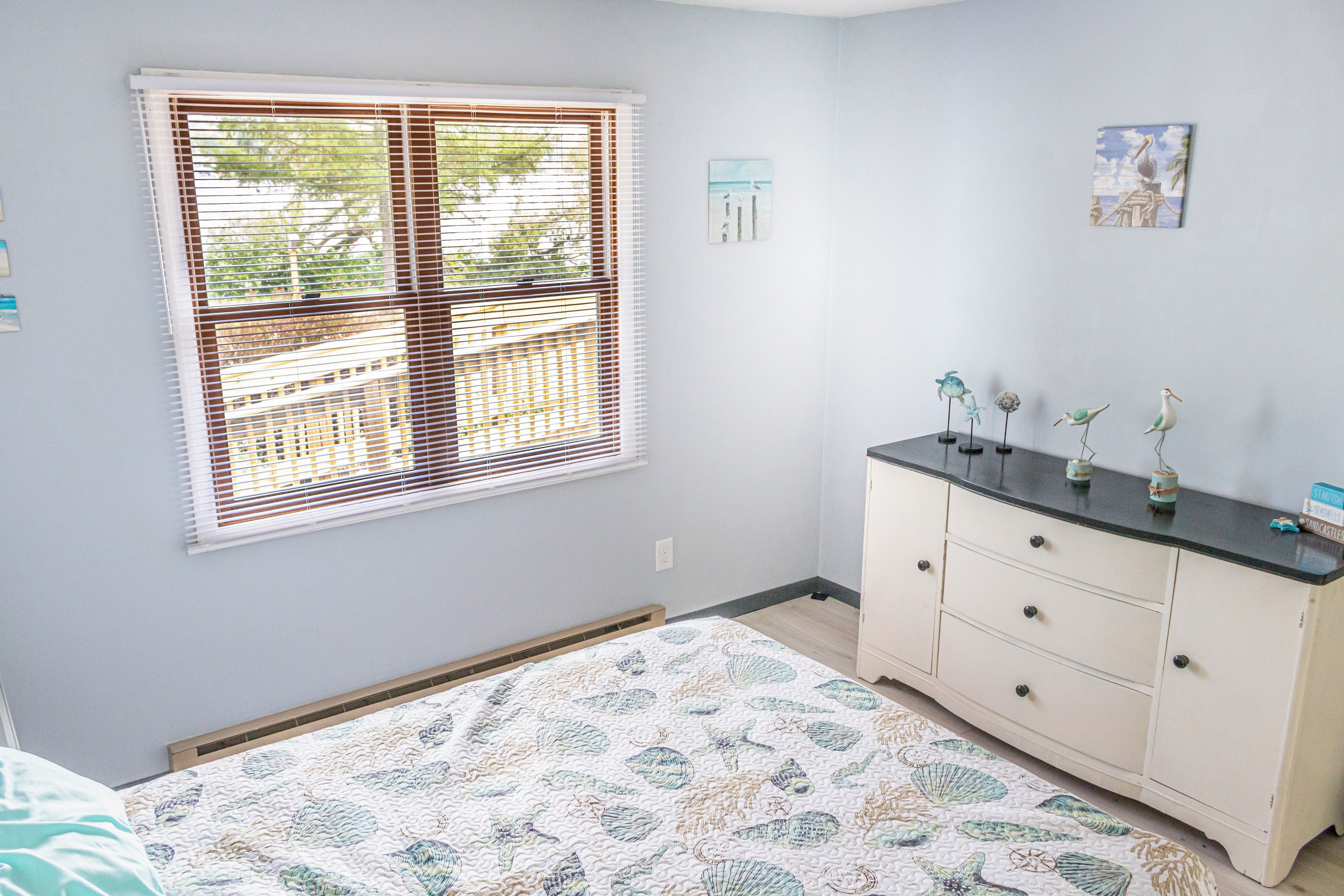 A bedroom with a bed, a dresser, a window with blinds, and wall art.
