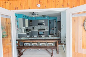 Ein Essbereich mit Holztisch und Metallstühlen, eine Küche mit Mikrowelle und Herd sowie eine blaue Wand mit dekorativen Fliesen.