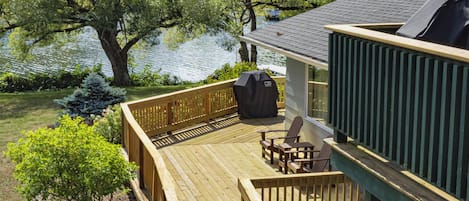 A wooden deck with a built-in barbecue grill, outdoor seating, and a view of a lake.