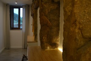 A room with a large rock wall, a wooden bench, and a window with curtains.