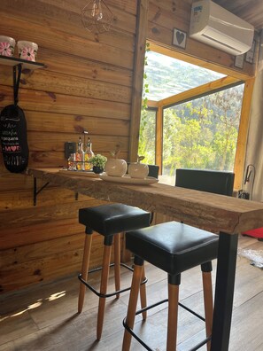 A wooden interior with a bar area, stools, and a view of greenery outside. - My eucalyptus cabin—a little piece of paradise. (Alfredo Wagner)