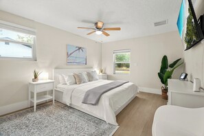 A bedroom with a bed, bedside tables, a ceiling fan, a window, a wall-mounted TV, and a potted plant. - Modern Home w/ Heated Pool, Spa + Putting Green (Sarasota)