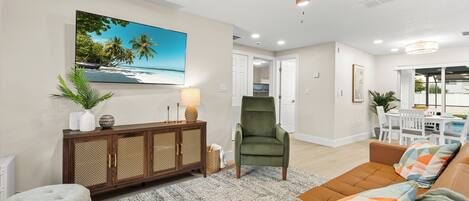 A living room with a ceiling fan, a large TV, a sofa, a chair, and a dining area with a table and chairs.
