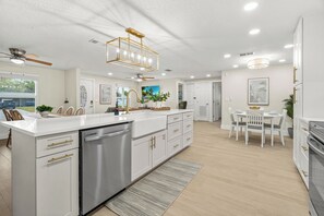 A modern kitchen with white cabinetry, stainless steel appliances, and a central island. - Modern Home w/ Heated Pool, Spa + Putting Green (Sarasota)