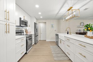 A modern kitchen with white cabinetry, stainless steel appliances, and a light wood floor. - Modern Home w/ Heated Pool, Spa + Putting Green (Sarasota)