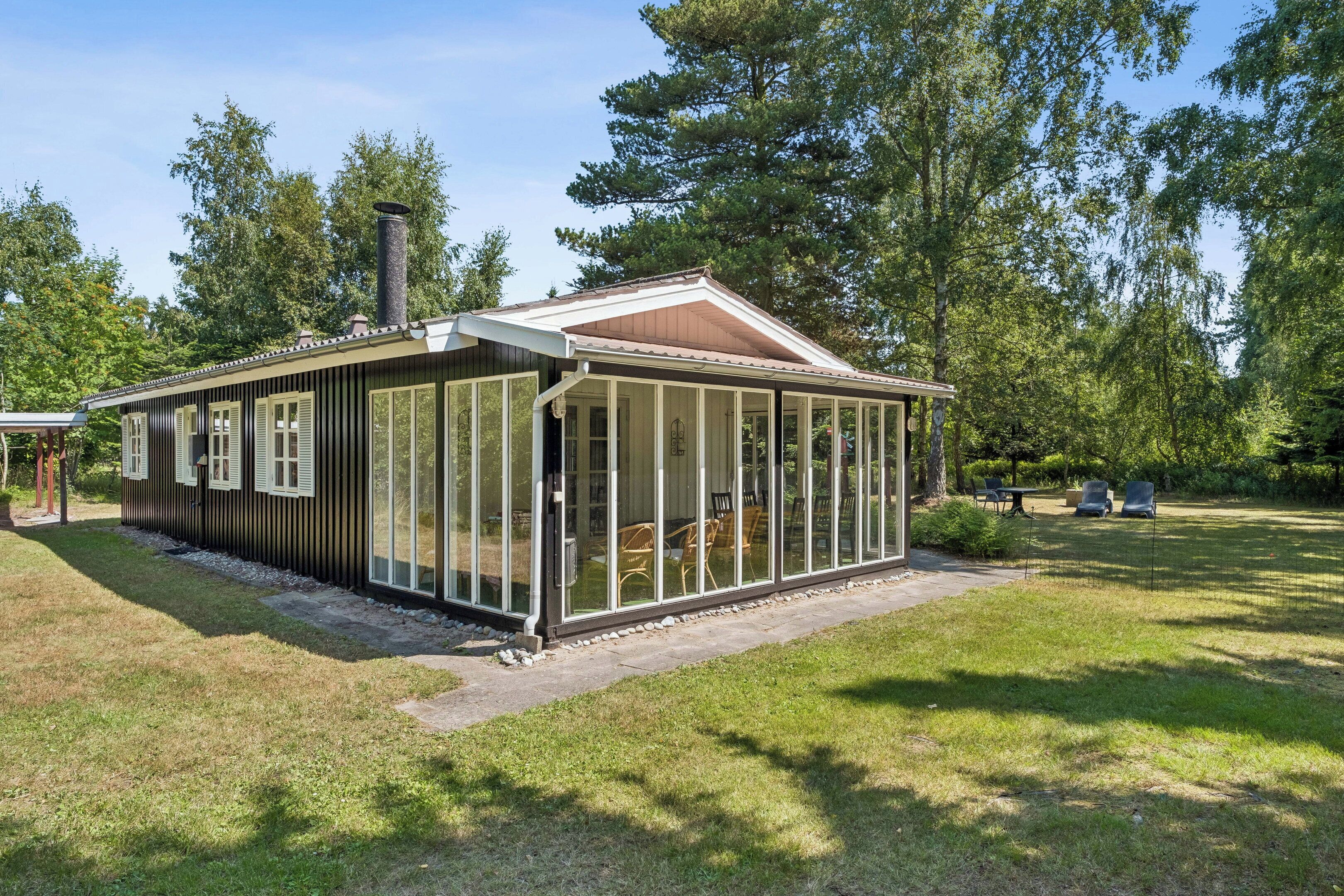 Une maison de plain-pied avec une véranda fermée par des baies vitrées, une cheminée et une pelouse bien entretenue.