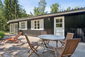 Ein Holzgebäude mit einer Terrasse, auf der ein Tisch und vier Stühle stehen.