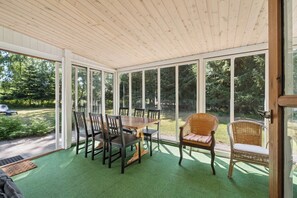 Eine überdachte Terrasse mit Esstisch und Stühlen, großen Fenstern und Blick auf eine grüne Landschaft.