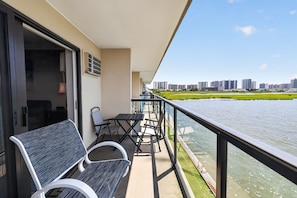 A balcony with a table and chairs, overlooking a body of water and a cityscape. - Bayfront 1BR With Pool Near Beach (Ocean City)