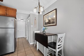 A kitchen with a refrigerator, a dining table with chairs, a chandelier, and a framed picture on the wall. - Bayfront 1BR With Pool Near Beach (Ocean City)