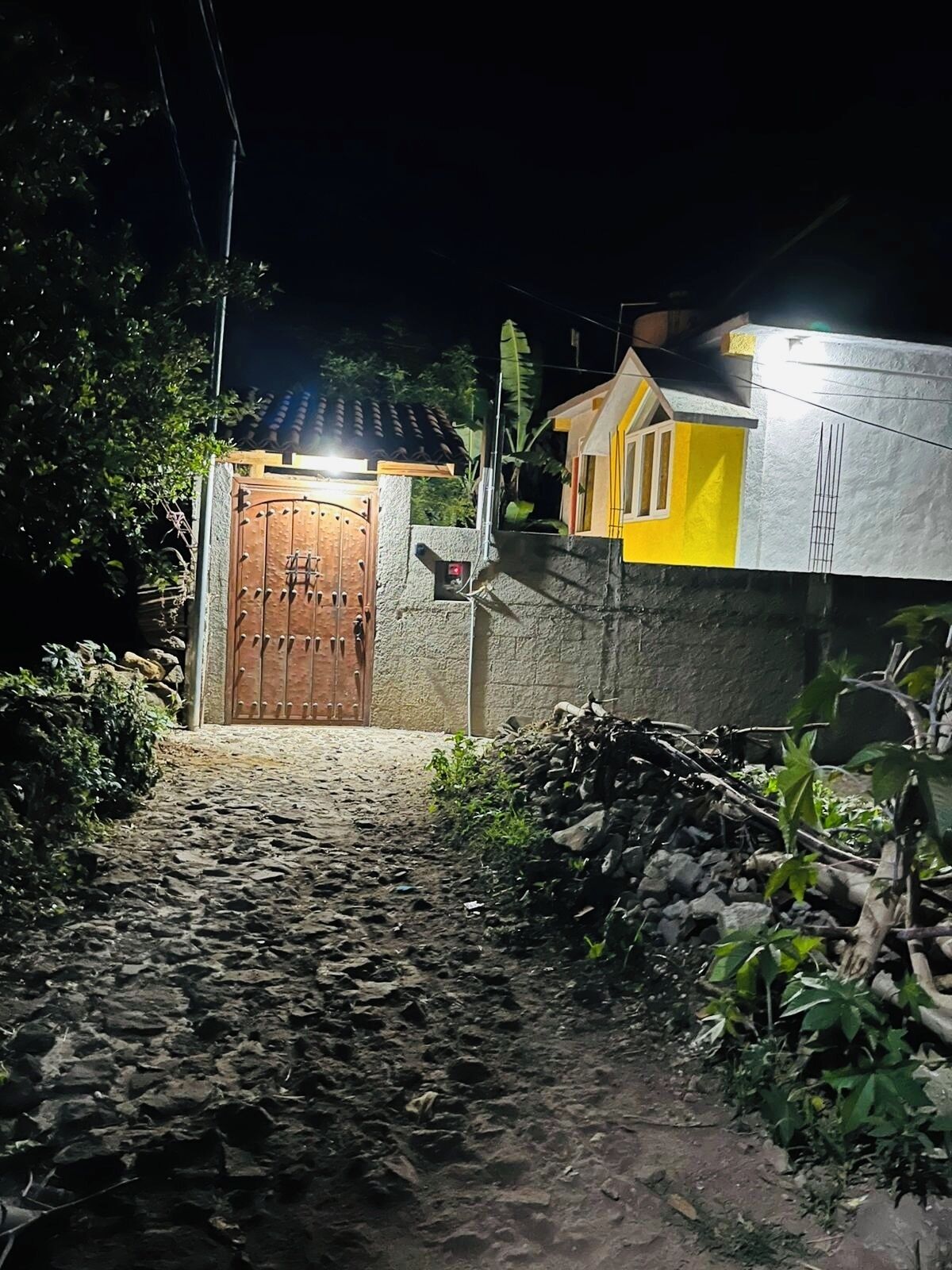 Una entrada con reja y un camino empedrado que lleva a una casa de fachada amarilla y puerta marrón.