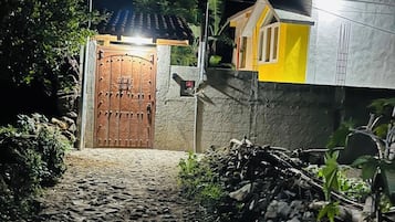 Una entrada con reja y un camino empedrado que lleva a una casa de fachada amarilla y puerta marrón.