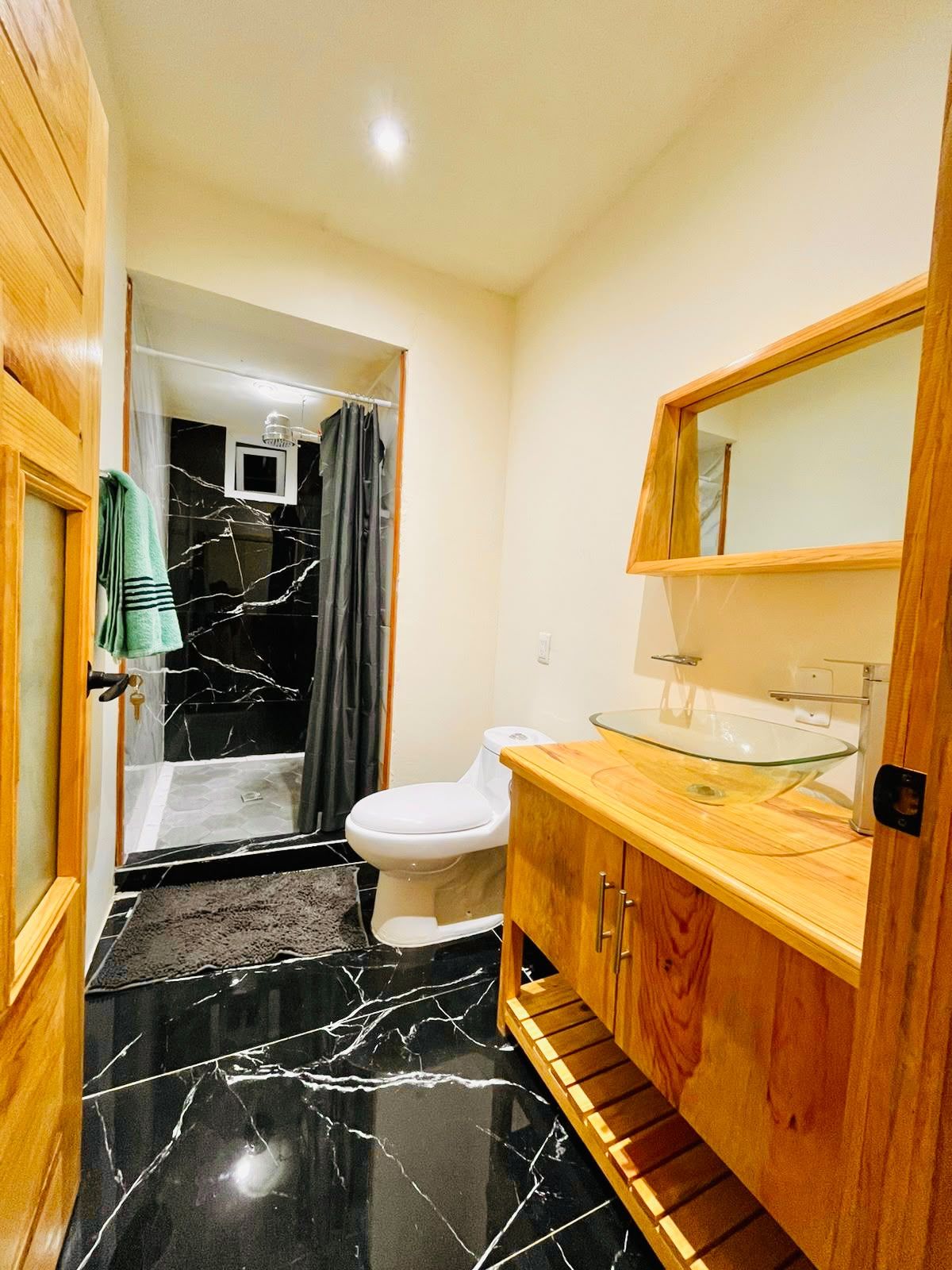 A bathroom with a glass shower enclosure, a white toilet, a wooden vanity with a glass sink, and a marble floor.