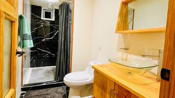 A bathroom with a glass shower enclosure, a white toilet, a wooden vanity with a glass sink, and a marble floor.